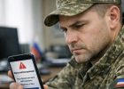 Военнослужащий в форме смотрит на экран смартфона с уведомлением о блокировке банковской карты